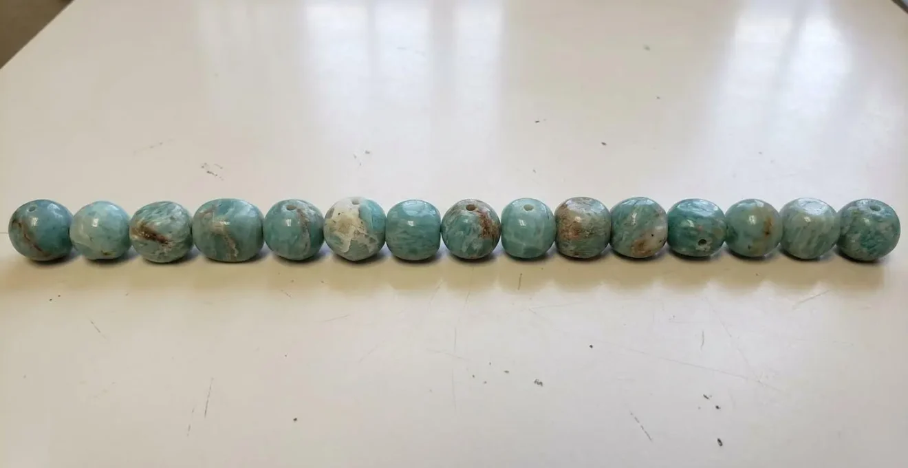 Gros plan en macrophotographie sur des perles d'amazonite naturelles alignées côte à côte révélant de subtiles variations de taille sur une surface blanche immaculée